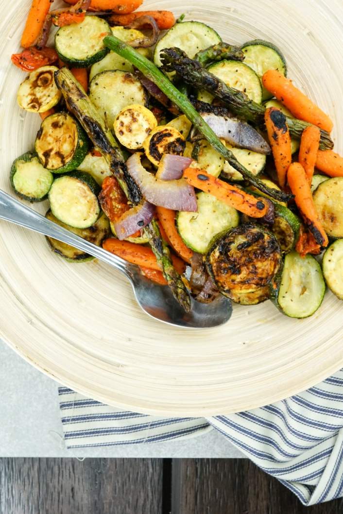 Grilled vegetables ready to be served on a platter with a spoon.