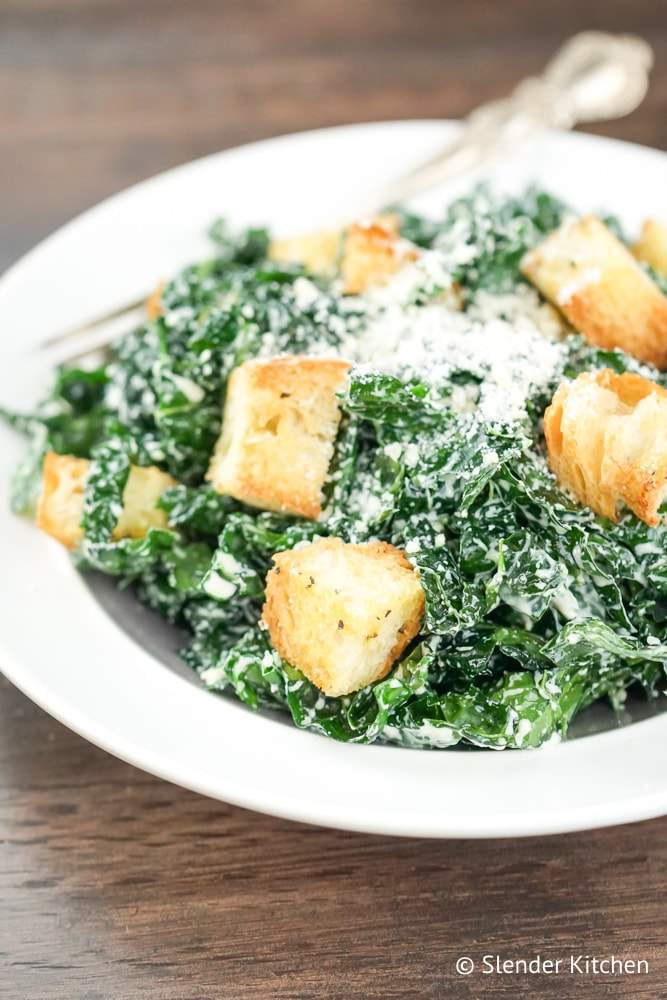 Kale Caesar Salad recipe on a white plate with a wooden background.