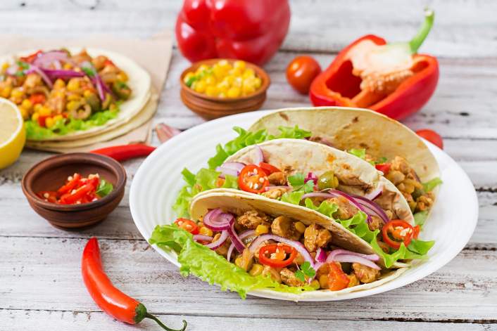 Spicy Chicken and Corn Tacos on a cutting board with a red pepper.