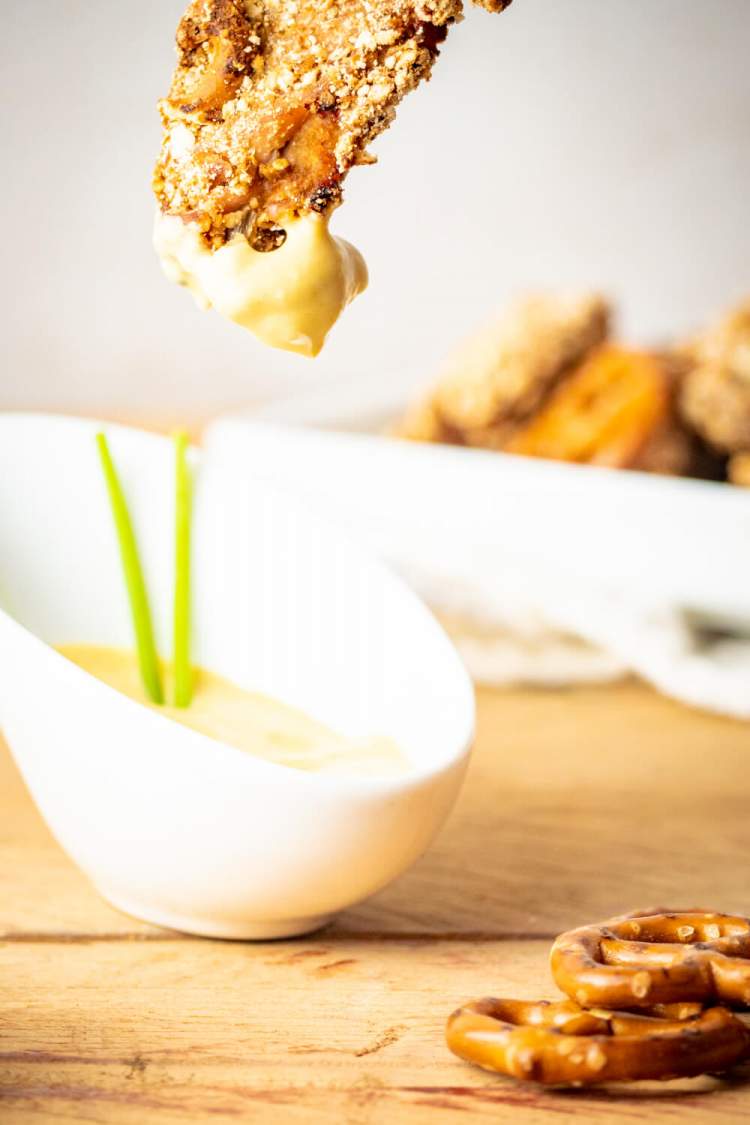 Pretzel chicken tenders being dipped in honey mustard dressing.