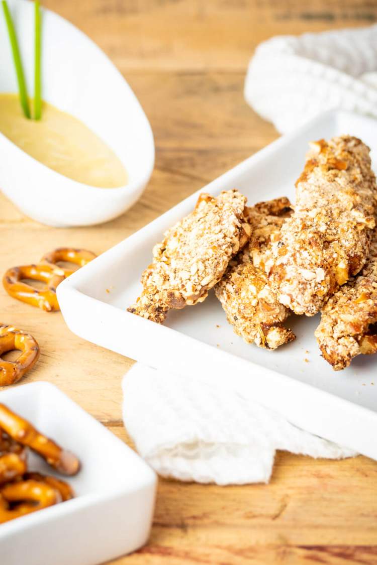 Pretzel coated chicken fingers on a plate with honey mustard on the side.