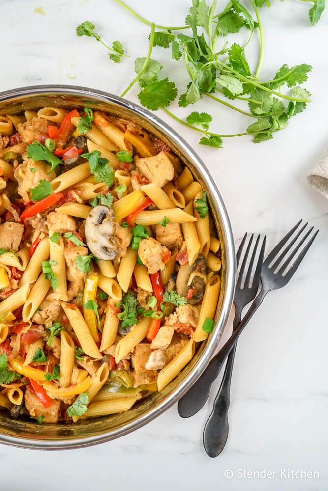 Chicken Fajita Pasta in a pan with peppers, onions, tomatoes, and mushrooms with cilantro on the side.