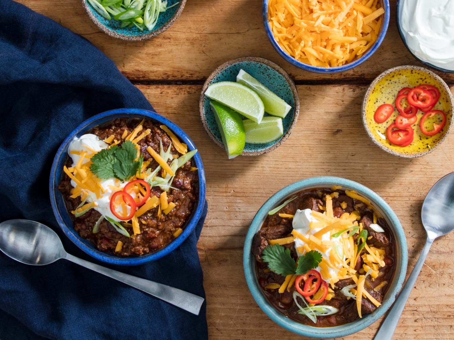 Two bowls of chili with lots of accompaniments