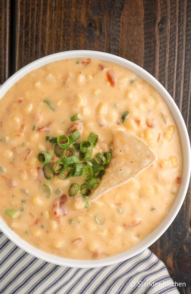 Corn dip with tomatoes, jalapenos, corn, and cheddar cheese in a bowl.