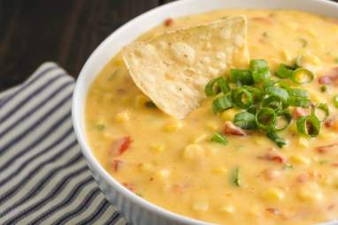 Corn dip with cheddar cheese, tomatoes, jalapeno, onion, and corn in a bowl.