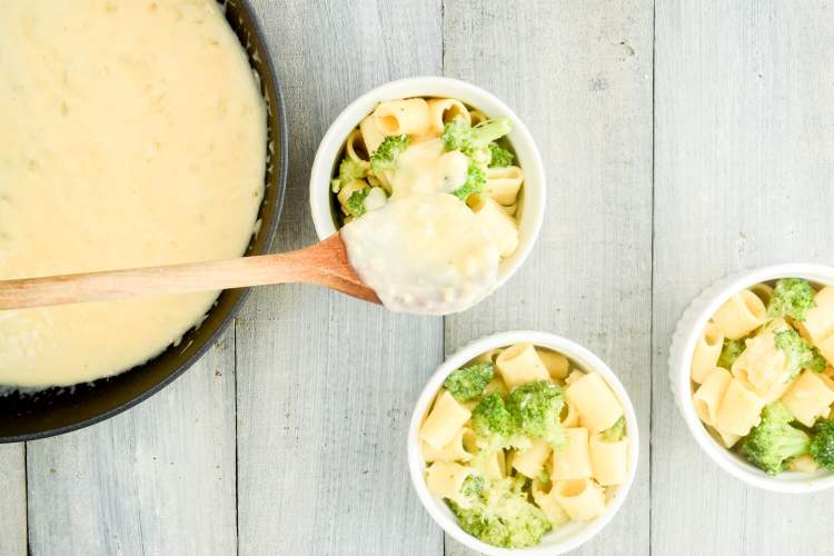 Baked broccoli macaroni and cheese wit cheese sauce being added to pasta and broccoli in small dishes.