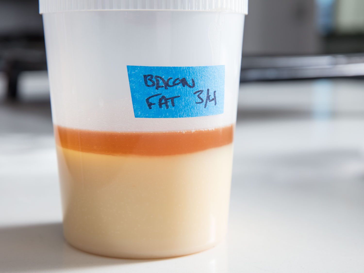A plastic container of partly solidified bacon fat, labeled 