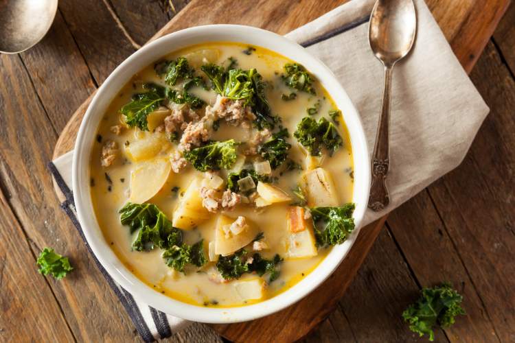 Kale soup with potatoes and sausage in a bowl on a wooden table.