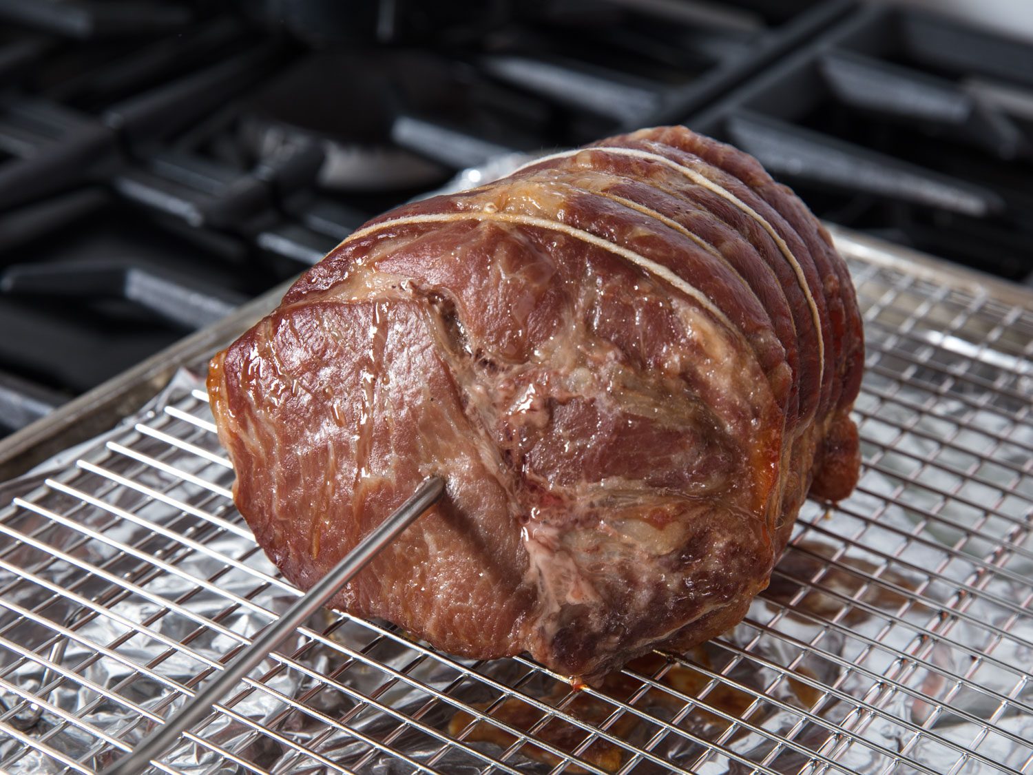 Side view of pork shoulder roast placed on rack set in rimmed baking sheet with temperature probe
