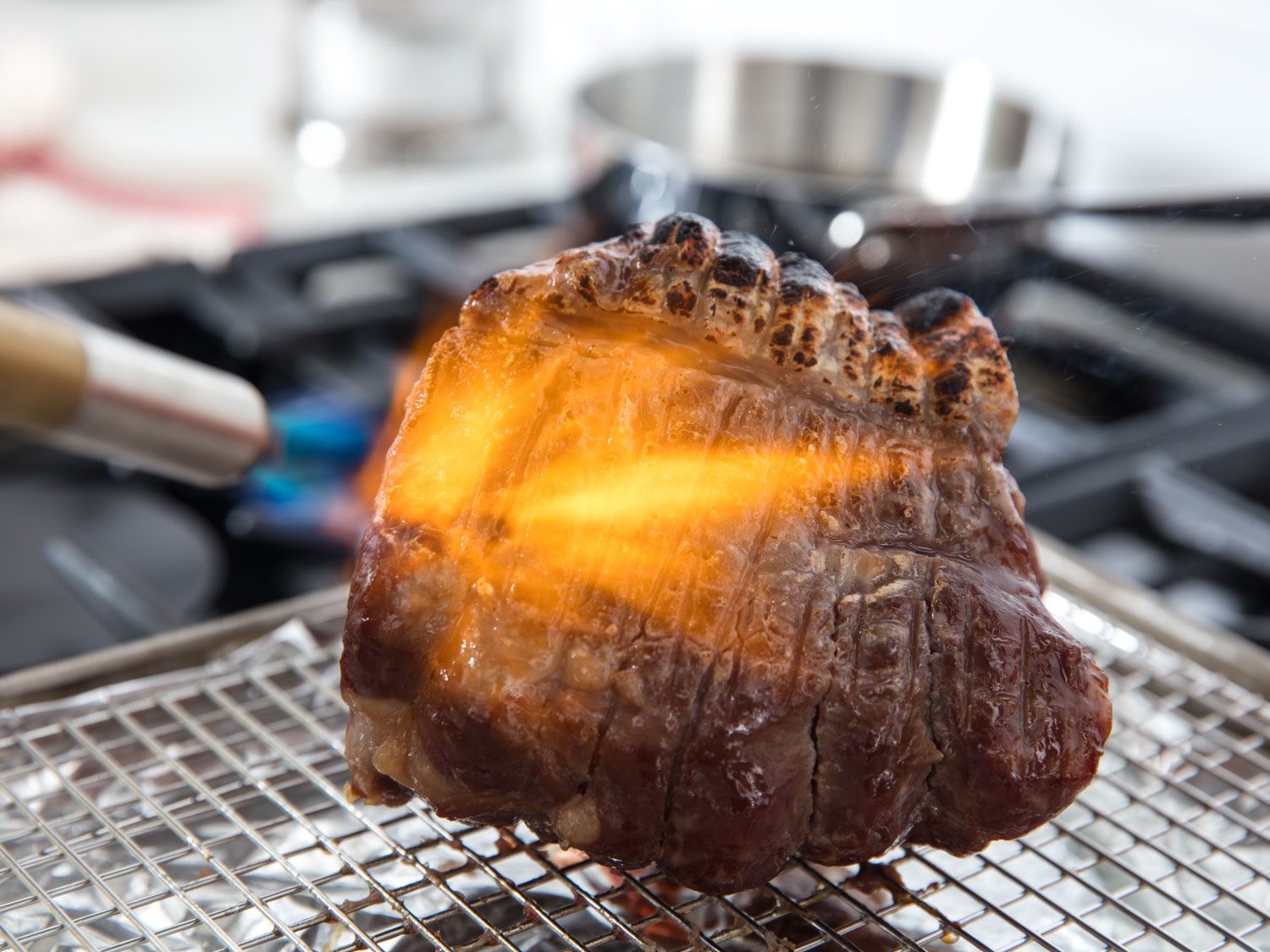 Handheld torch charring exterior of pork shoulder chashu roast