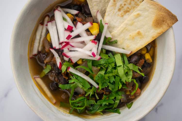 Bowl of tortilla soup with beans and corn with tortilla strips and cilantro.