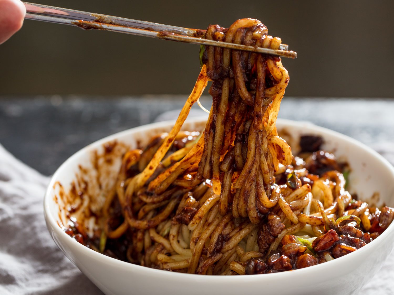 Chopsticks lifting a twirl of jjajangmyeon (noodles in black bean sauce)