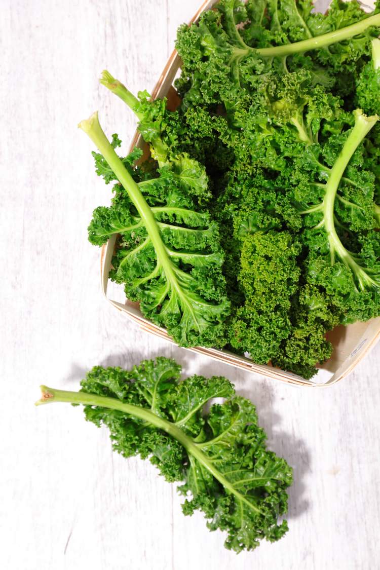 Pieces of curly kale scattered on a white wood background.