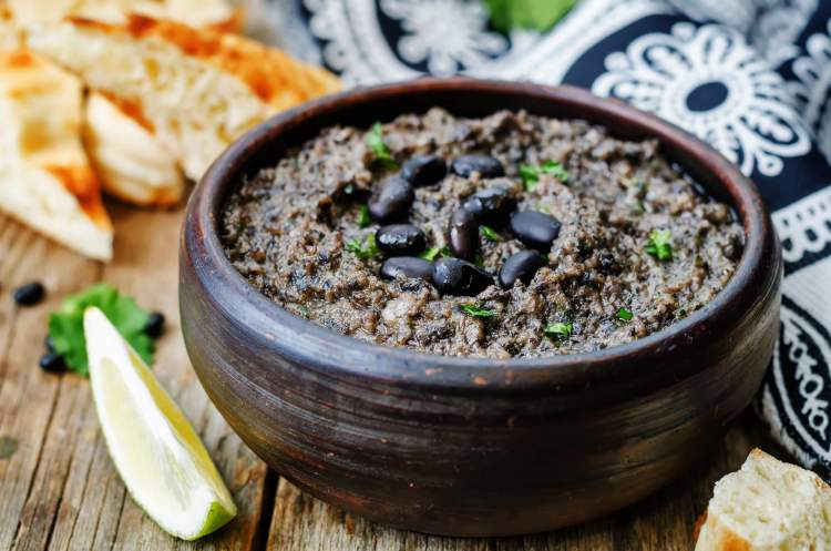 Black bean hummus with cilantro and limes on a wooden board.