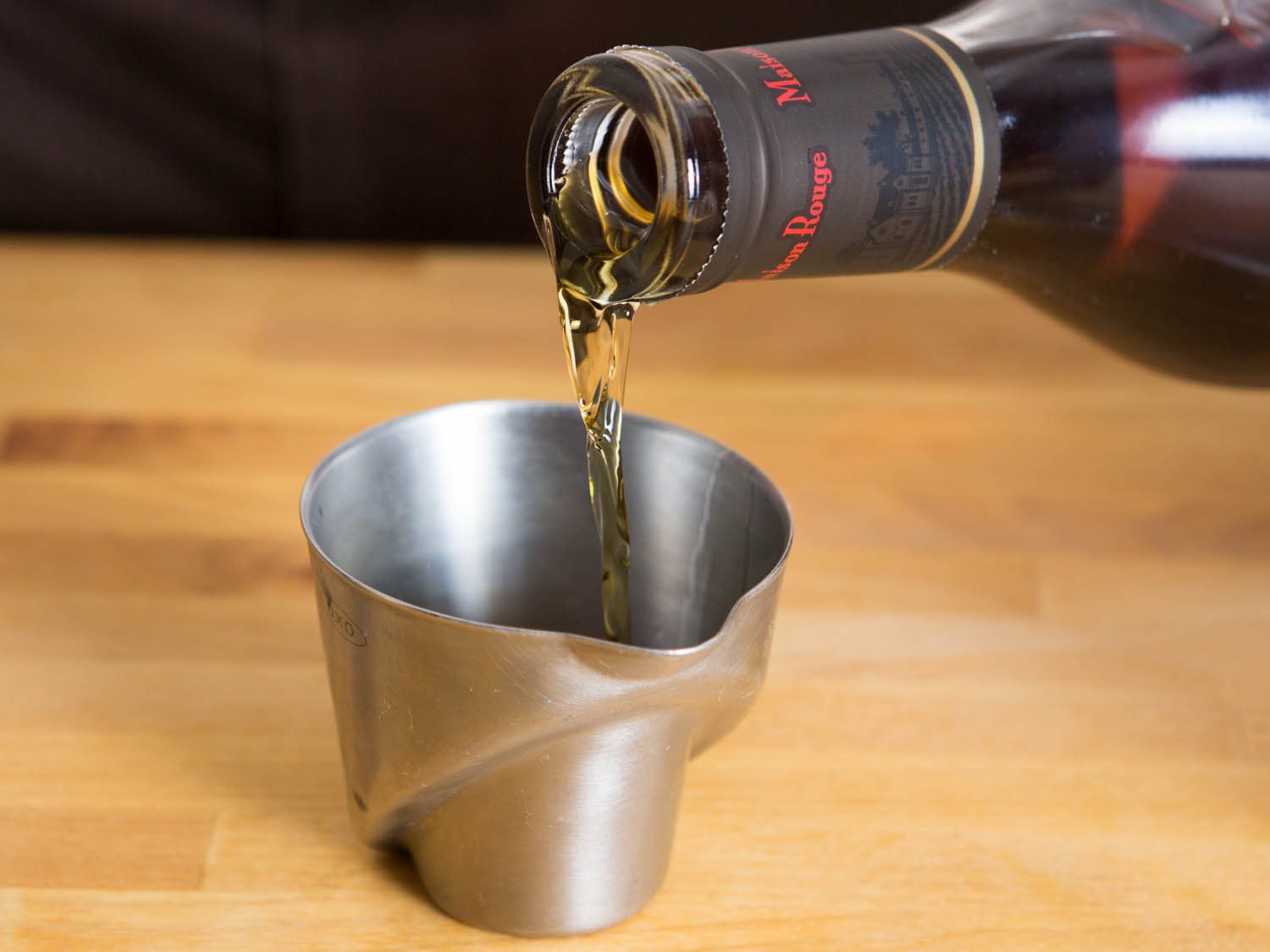 Pouring from a bottle into a miniature metal measuring cup