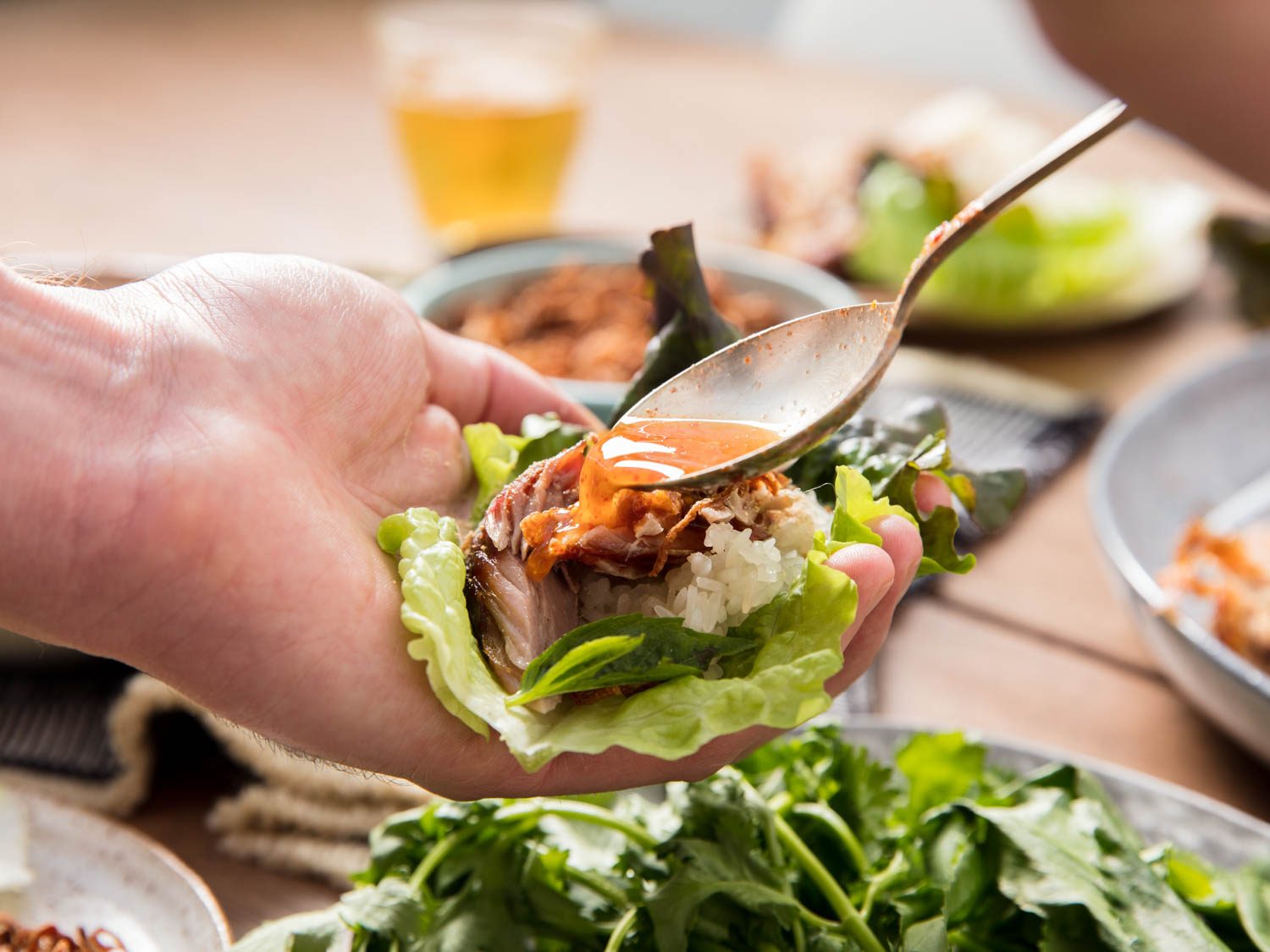 Spooning dipping sauce over a lettuce wrap with pork, sticky rice, and herbs.