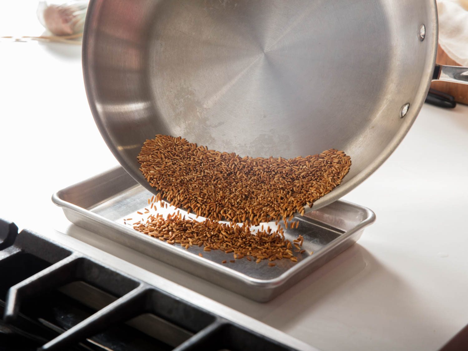 Transferring toasted rice from a skillet to a small baking sheet to cool.
