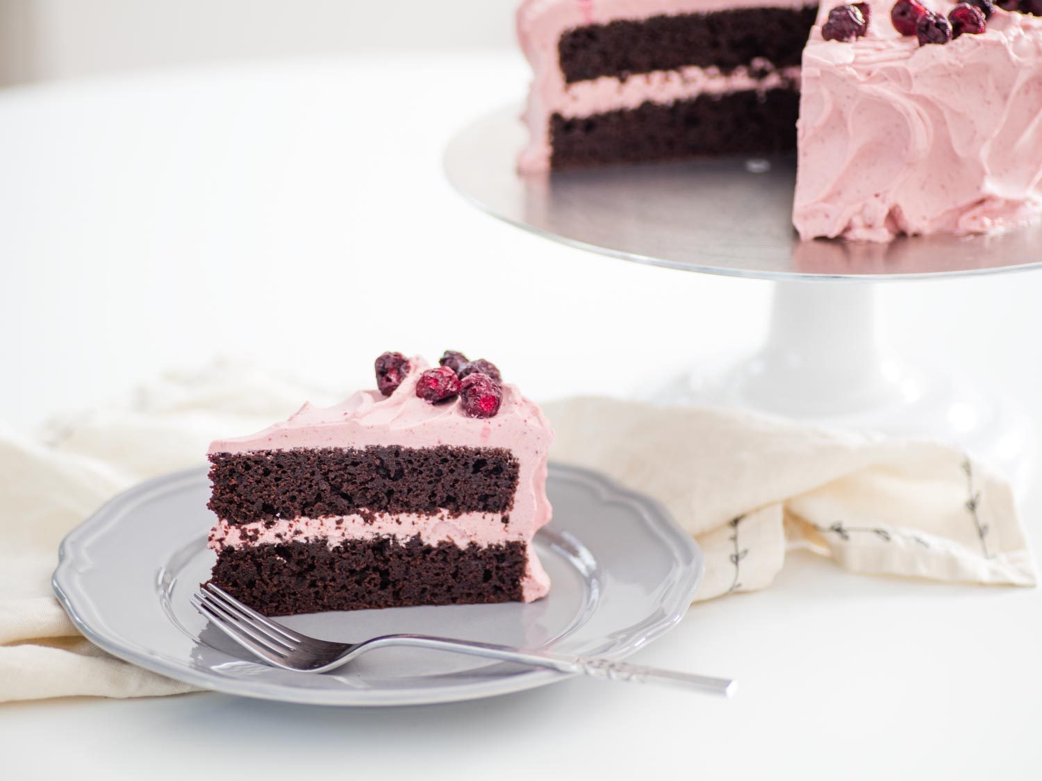 A slice of chocolate cherry layer cake on a plate, next to the rest of the cake on a cake stand