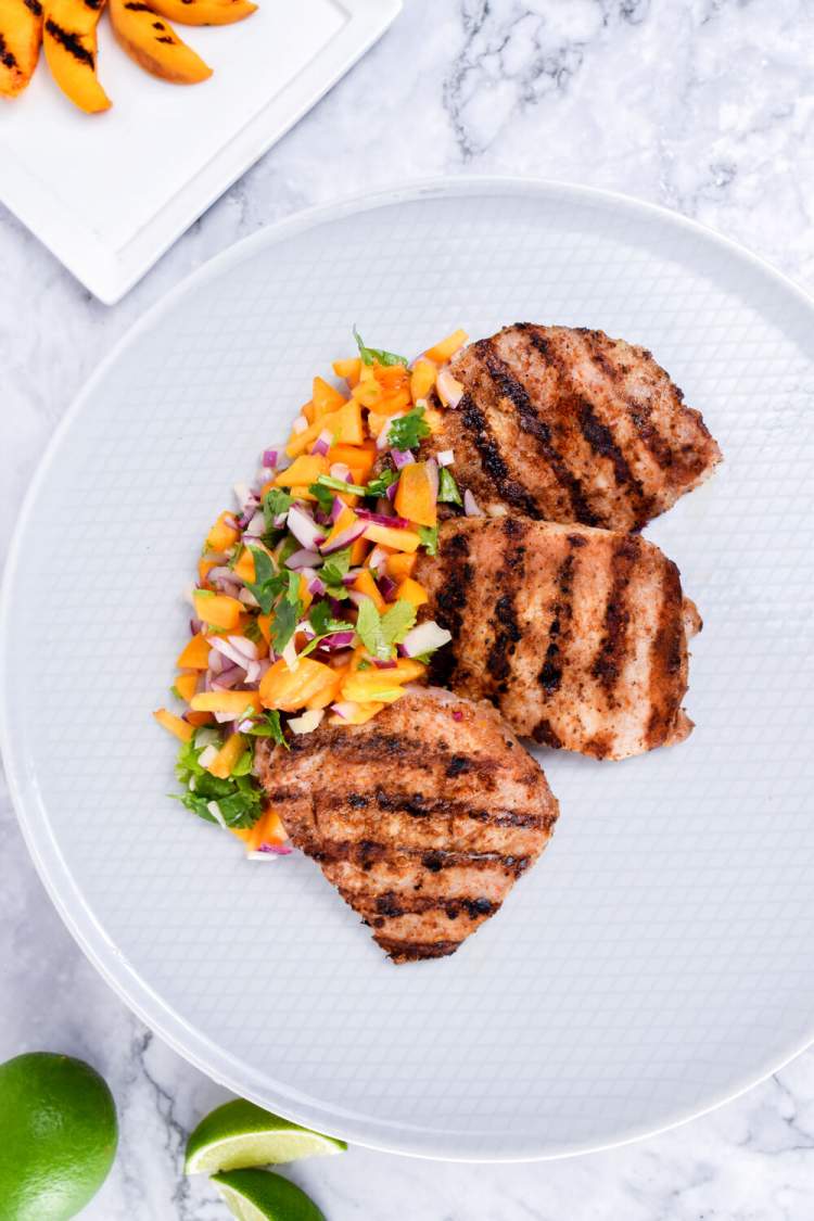 Grilled pork with grilled peaches and salsa on a white plate/