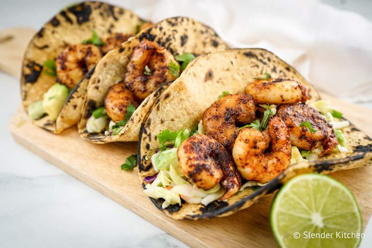 Easy shrimp tacos with cabbage slaw, limes, avocado, and cilantro on tortillas.