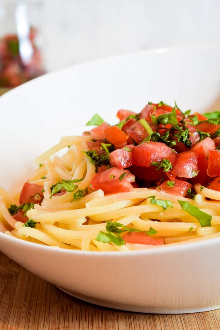 Pasta with fresh tomato sauce and chopped basil in a white bowl.