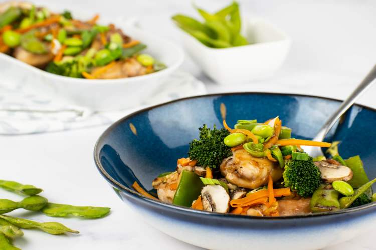 Chicken with soy sauce and vegetables in a bowl with a plate of chicken in the background.