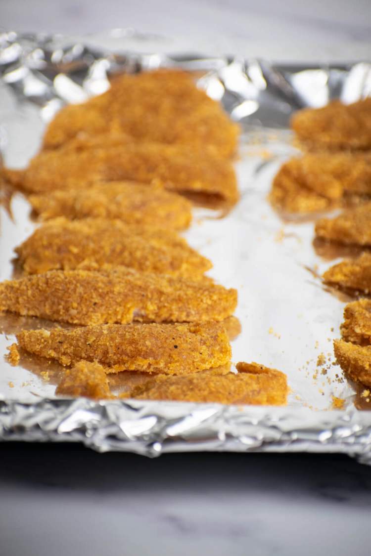 Almond crusted chicken fingers on a baking sheet covered in foil.