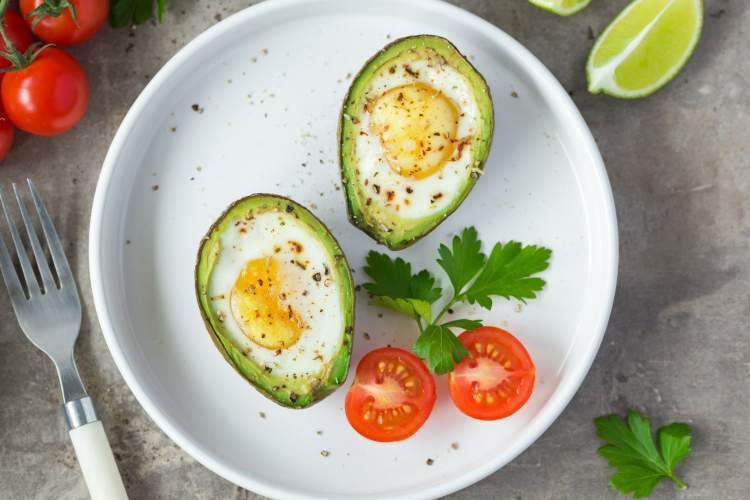 Whole30 Avocado Bakwed Eggs with salt, pepper, and cherry tomatoes.