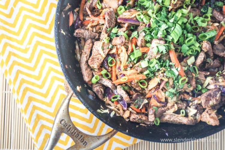 Moo shu beef stirfry with cabbage, thin slices of beef, and green onions in a skillet.