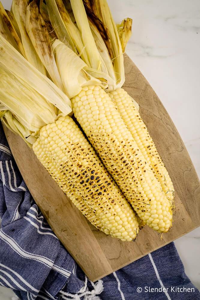 Best grilled corn with the husk attached and caramelized kernels on a cutting board.