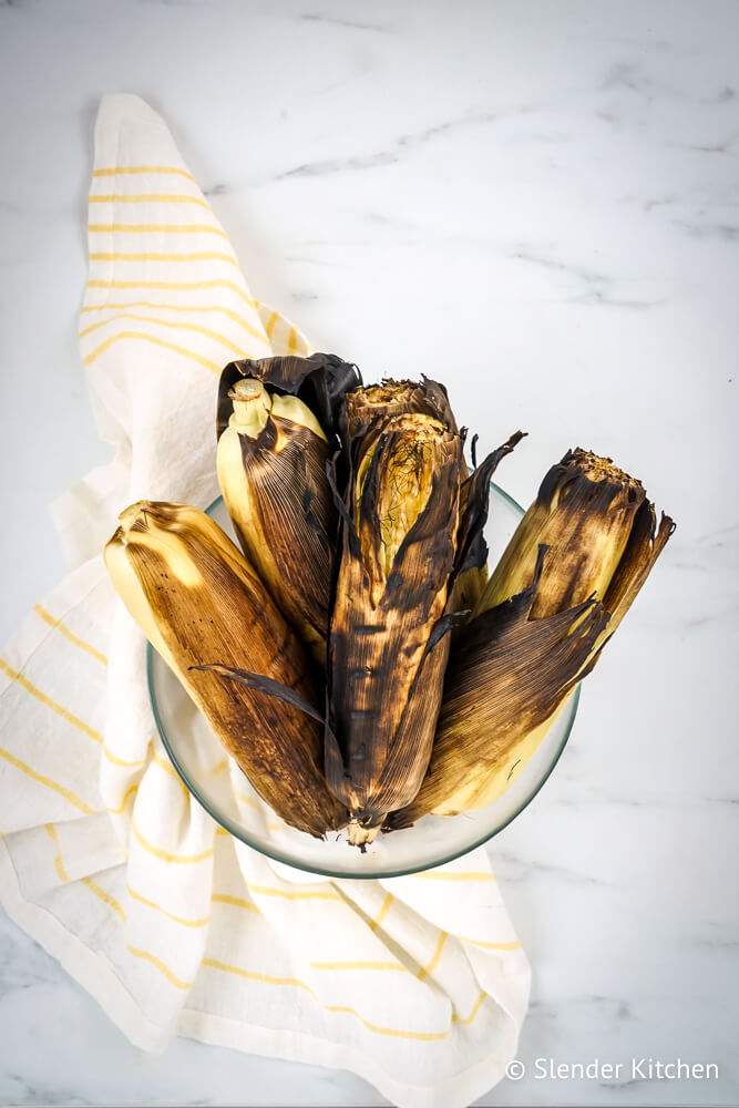 Easy grilled corn in the husk in a glass bowl with a napkin.