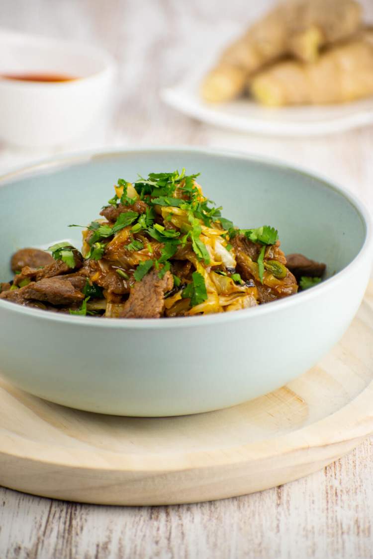 Moo shu stir fry with beef, cabbage, and green onions in a bowl with a spoon.