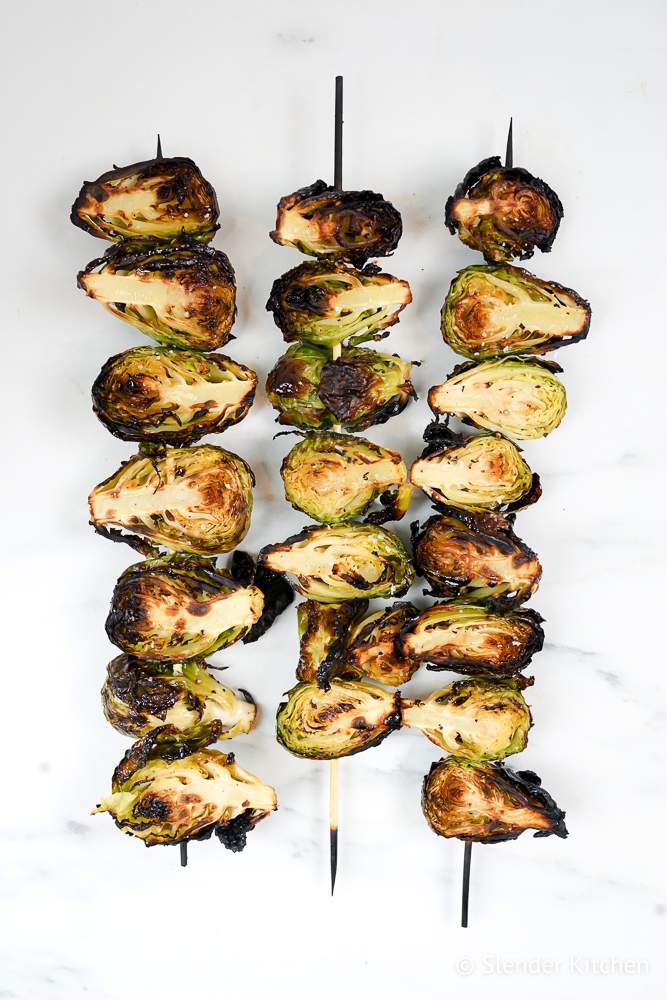 Grilled Brussels Sprouts on skewers with browned grill marks, olive oil, and salt.