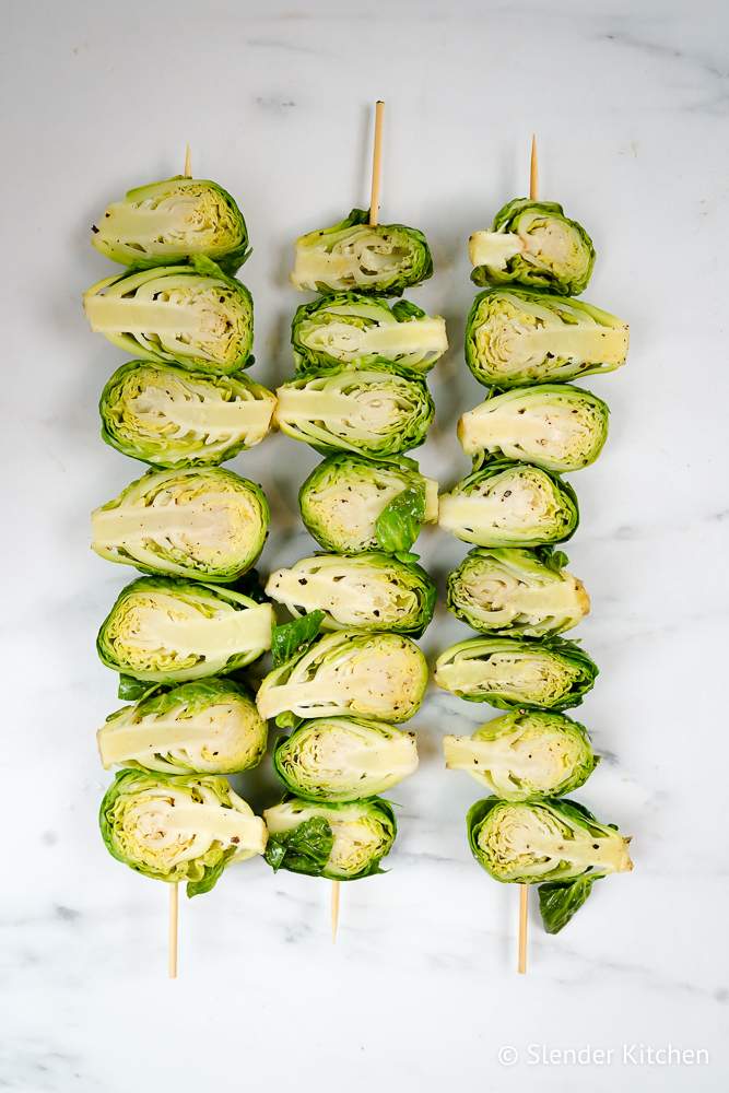 Grilling Brussels sprouts on a skewer with olive oil, salt, and pepper.