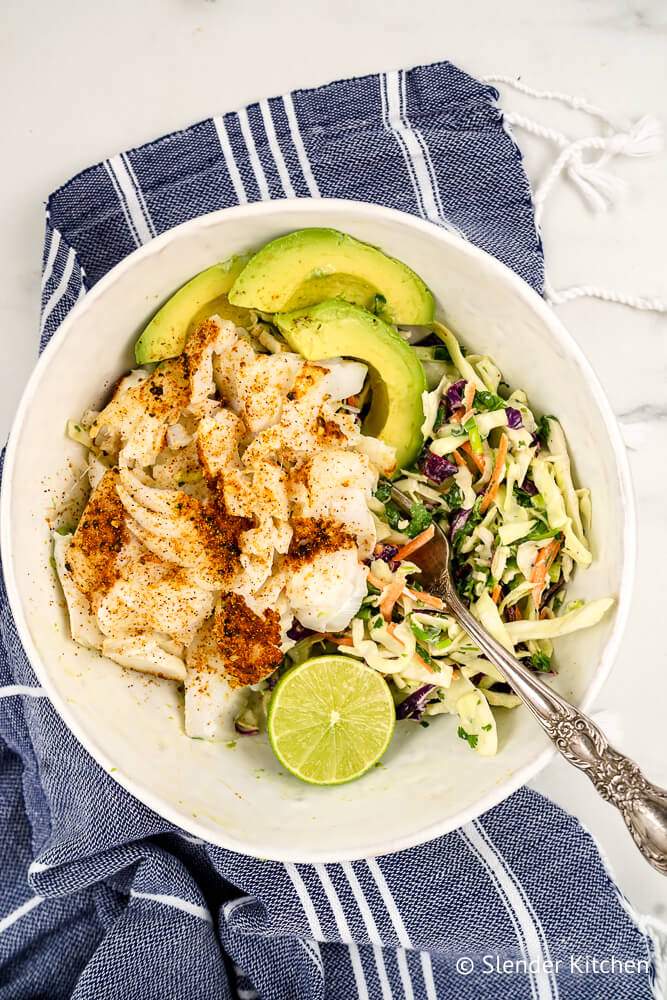 Low carb fish tacos with cod, creamy lime coleslaw, and avocado in a bowl with a fork.