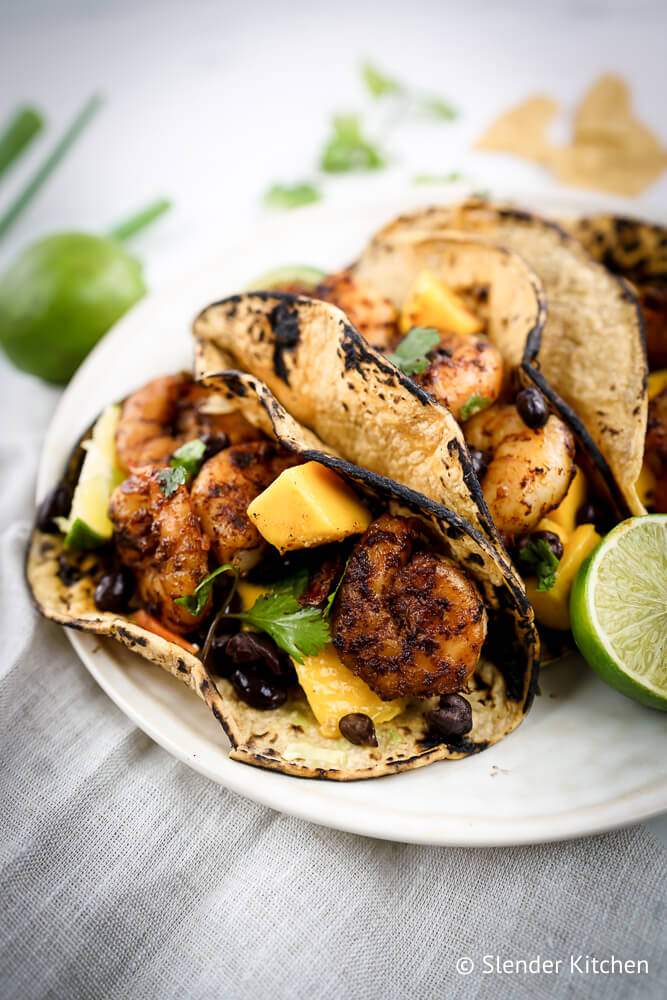 Shrimp tacos with mango salsa and black beans in corn tortillas with limes and green onions.