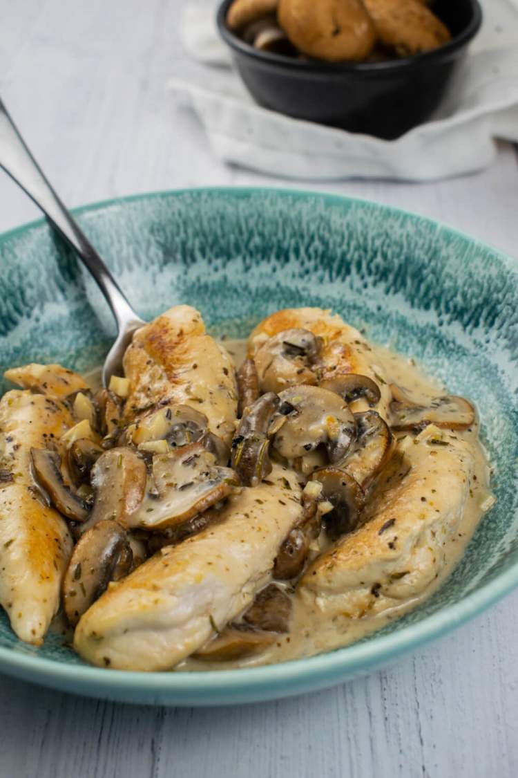 Mushroom chicken in garlic sauce in a blue bowl with a spoon.