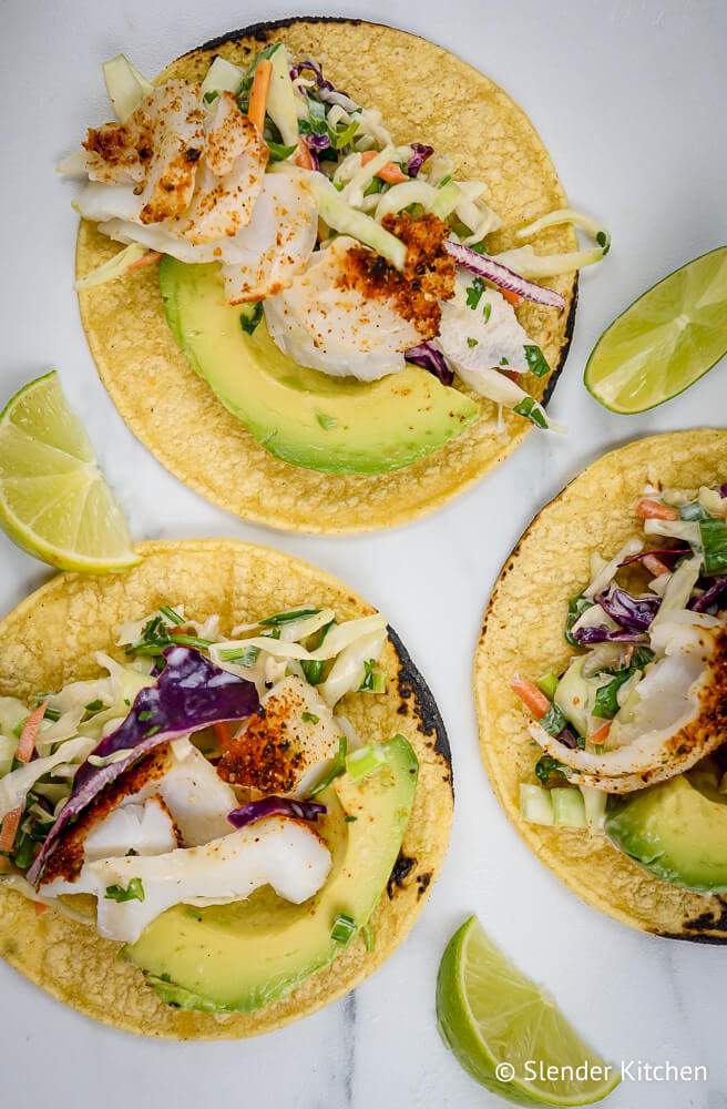 Mexican fish tacos with coleslaw, limes, and avocado in toasted tortillas.