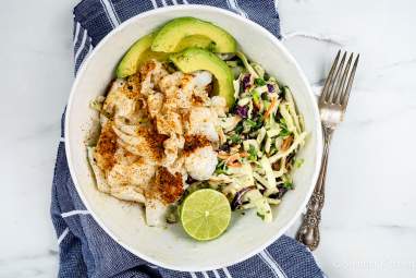 Ancho Fish Taco Bowls with Lime Slaw and Avocado Ancho fish taco bowl with lime slaw and sliced avocado with a blue napkin.