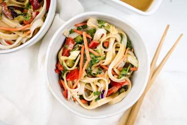 Asian noodle salad with almond dressing, rice noodles, and vegetables in a bowl with chopsticks.