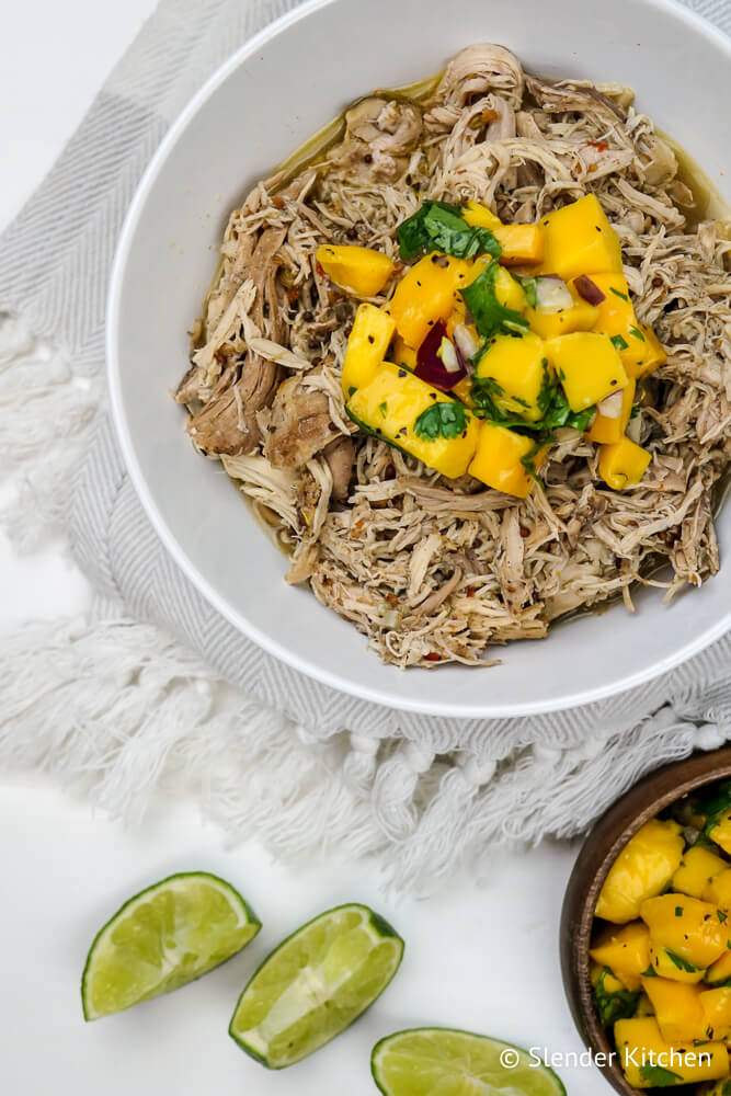 Crockpot jerk chicken shredded in a bowl with lime slices and mango salsa.