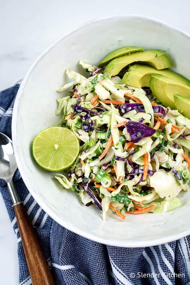 Mexican coleslaw in a bowl with cilantro, cabbage, fresh lime, and avocado.