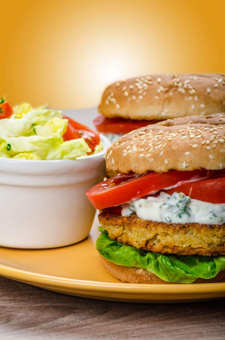 Chickpea burger with tomatoes, lettuce, and yogurt sauce on a plate.
