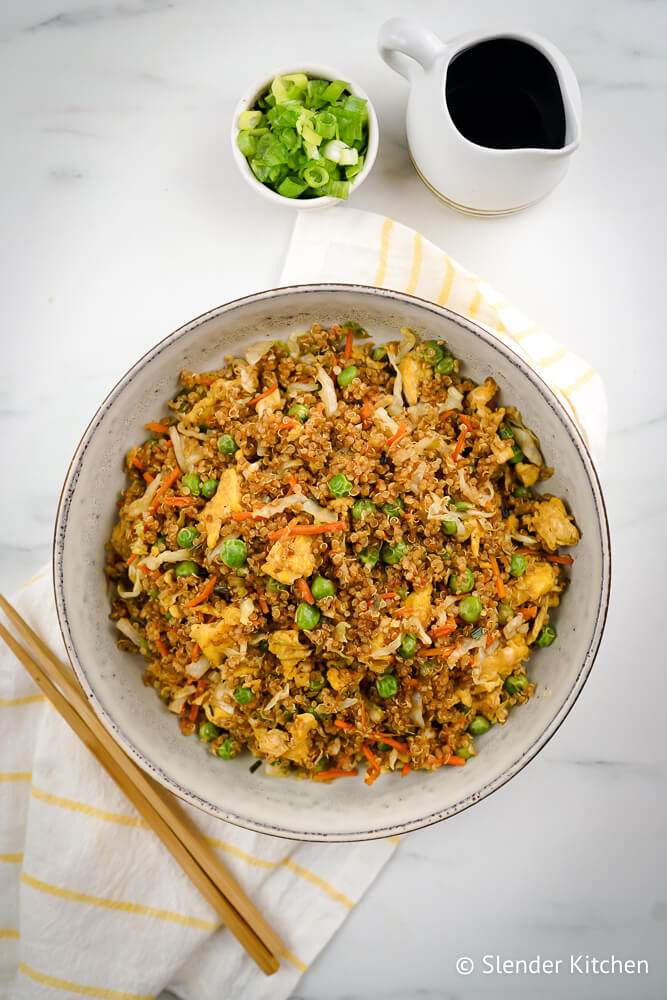 Fried rice with quinoa in a bowl with chopsticks, chopped green onions, cooke quinoa, eggs, and vegetables.