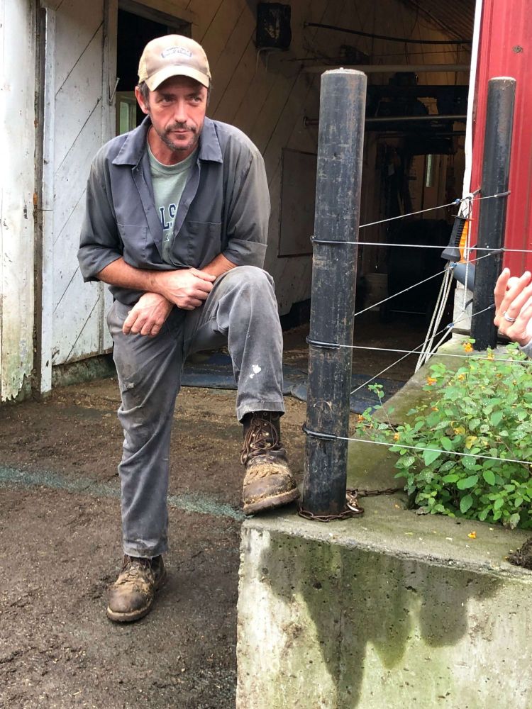 Farmer leaning down on his knee in front of a farm.