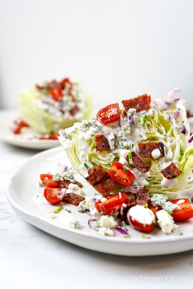 Wedge salad with blue cheese, bacon, tomatoes, and red onions on plate.