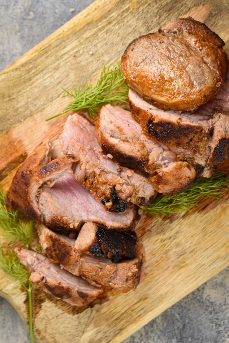 Barbecue pork tenderloin on a wooden cutting board with rosemary.