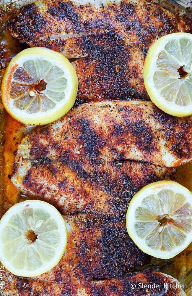 Baked blackened tilapia in a glass dish with lemon slices and blackening spices.