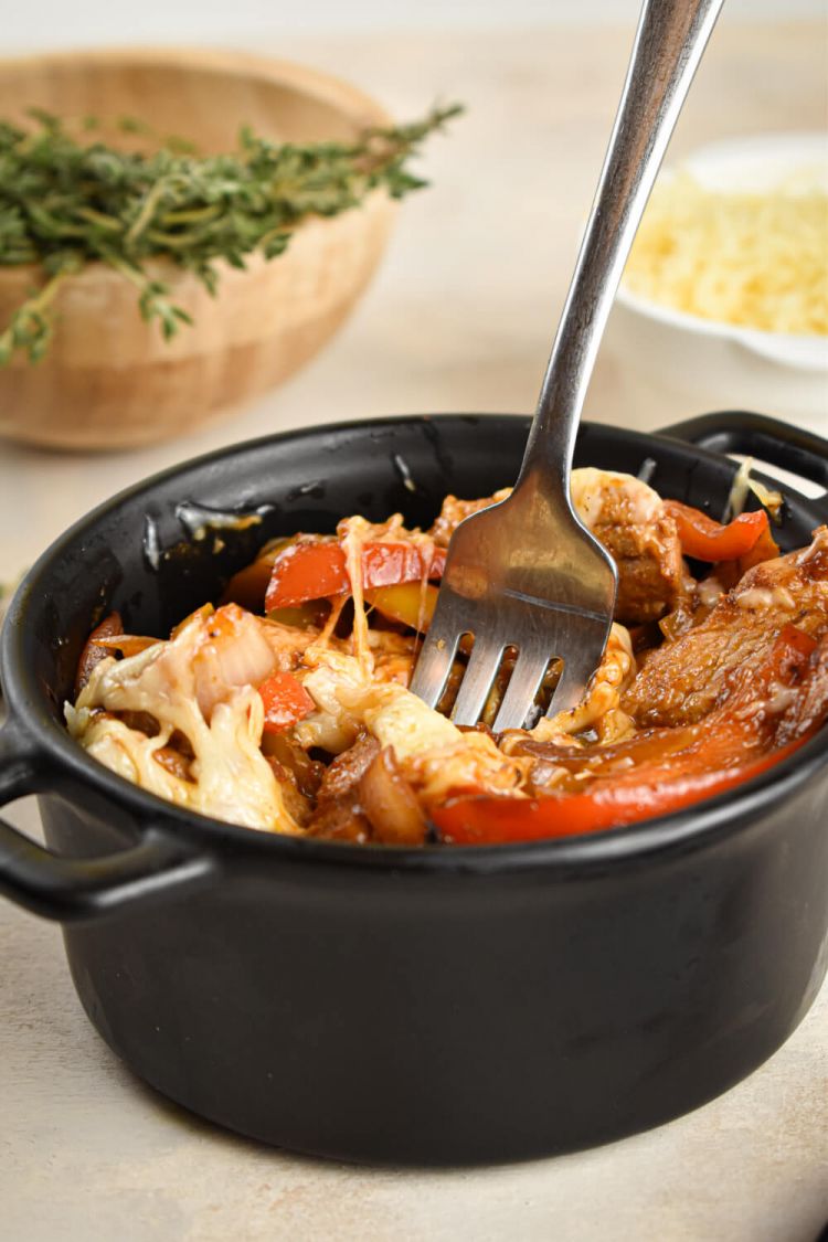 Easy pork and peppers in a cast iron ramekin with thyme, Parmesan cheese, and a fork.