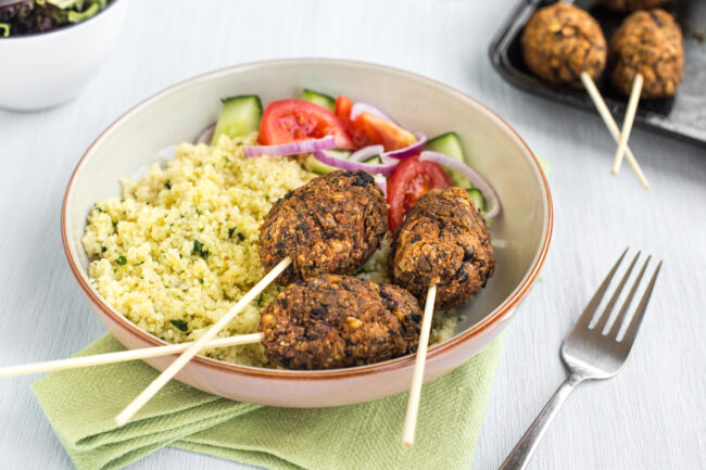 Vegetarian koftas on sticks, served in a bowl with couscous and tomato salad.